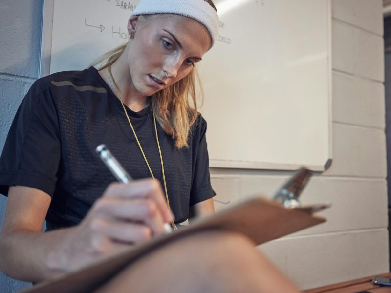 woman-sport-coach-and-clipboard-writing-of-an-athlete-writing-exercise-schedule-or-plan-personal.jpg